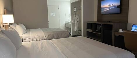 A hotel room with two beds, a TV, a desk with a computer, and a view of the beach.