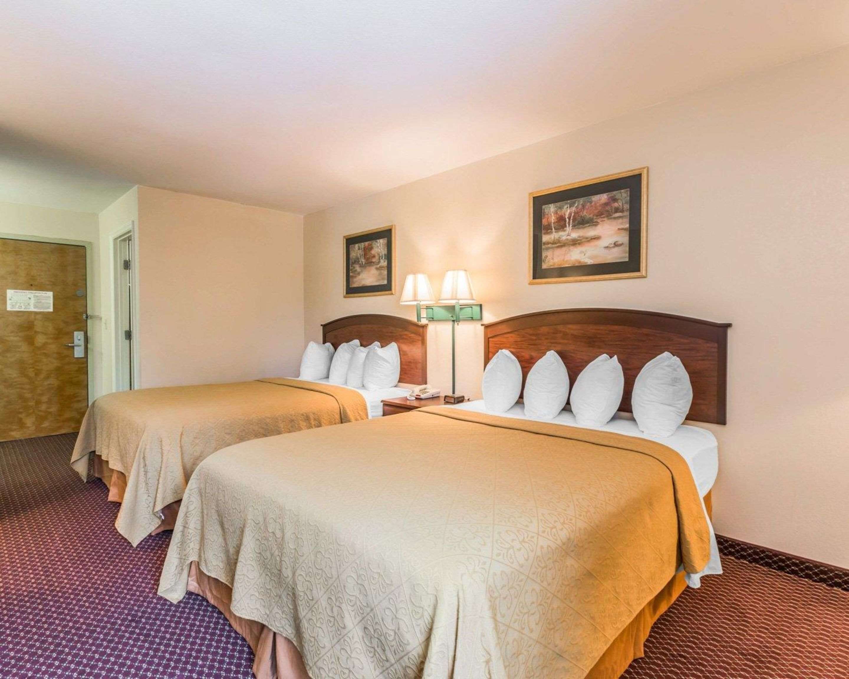 A hotel room with two beds, a nightstand, a lamp, and two framed pictures on the wall.