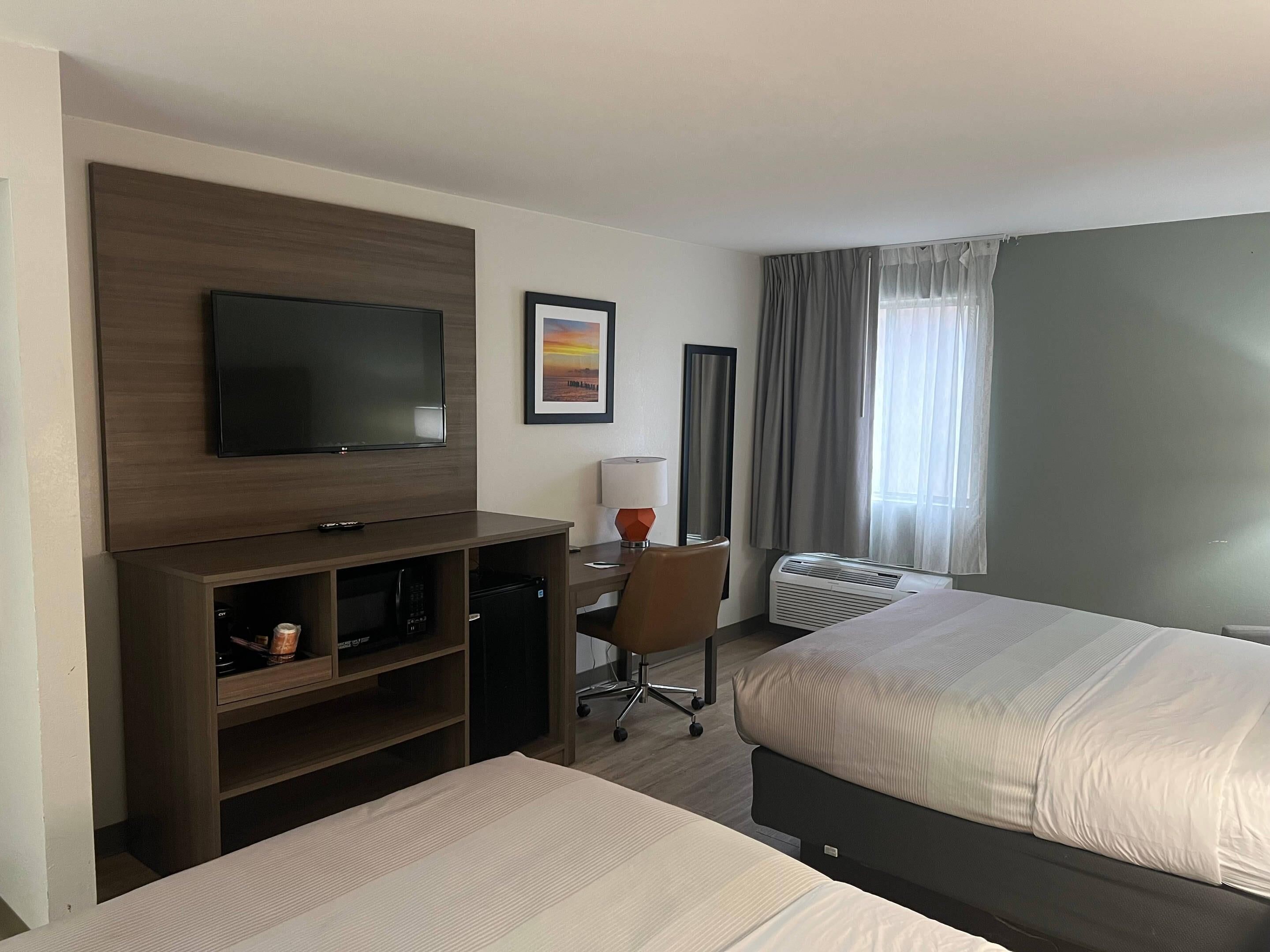 Een hotelkamer met een televisie, een bureau met lamp, een airconditioner en twee bedden.
