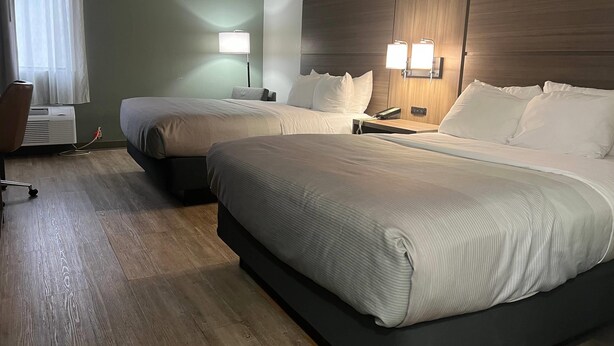 A hotel room with two beds, a desk, and a chair. There are two bedside tables with lamps.