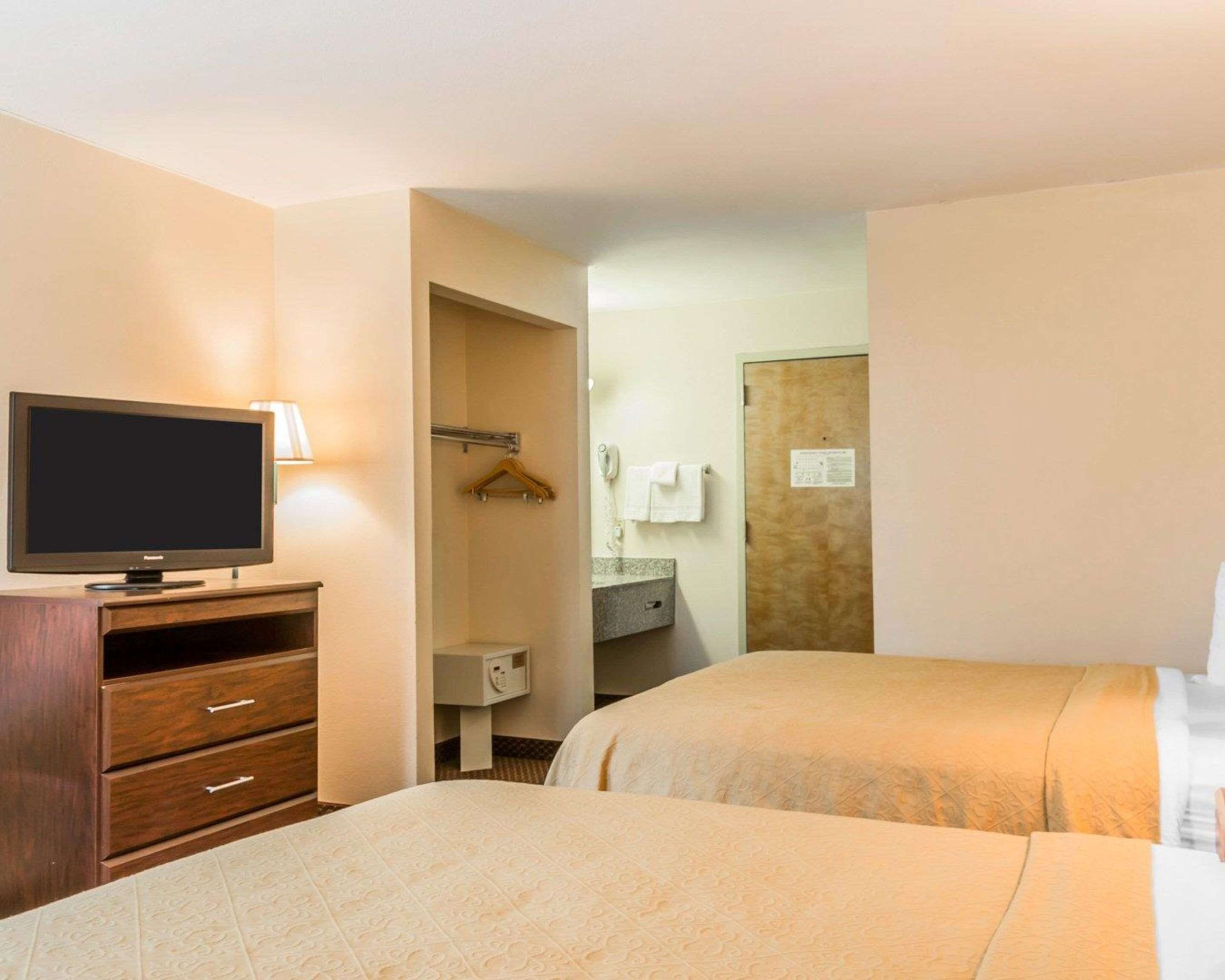 Habitación de hotel con dos camas, un televisor sobre un tocador de madera, un baño con toallero y un espejo.