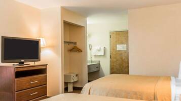 Habitación de hotel con dos camas, un televisor sobre un tocador de madera, un baño con toallero y un espejo.
