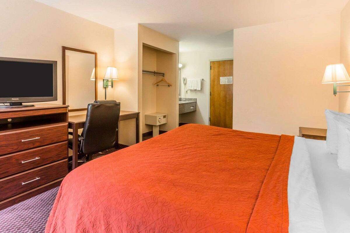 Une chambre d’hôtel avec un grand lit, une télévision, un bureau avec une chaise, un miroir et deux lampes.
