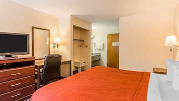 A hotel room with a large bed, a TV, a desk with a chair, a mirror, and two lamps.