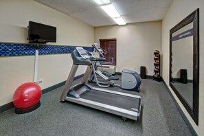 A fitness room with treadmills, a stationary bike, a red exercise ball, and a wall-mounted TV.