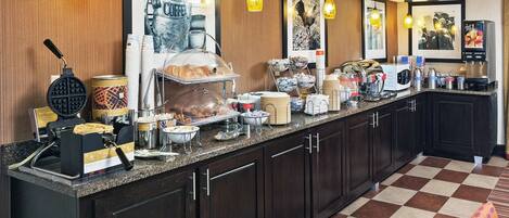 A buffet counter with various food items, a waffle maker, and a coffee station.