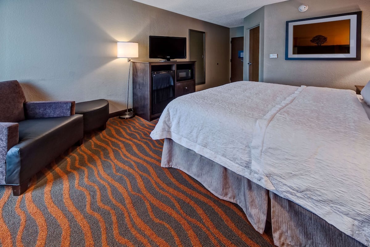 A hotel room with a large bed, a sofa, a TV, and a microwave.