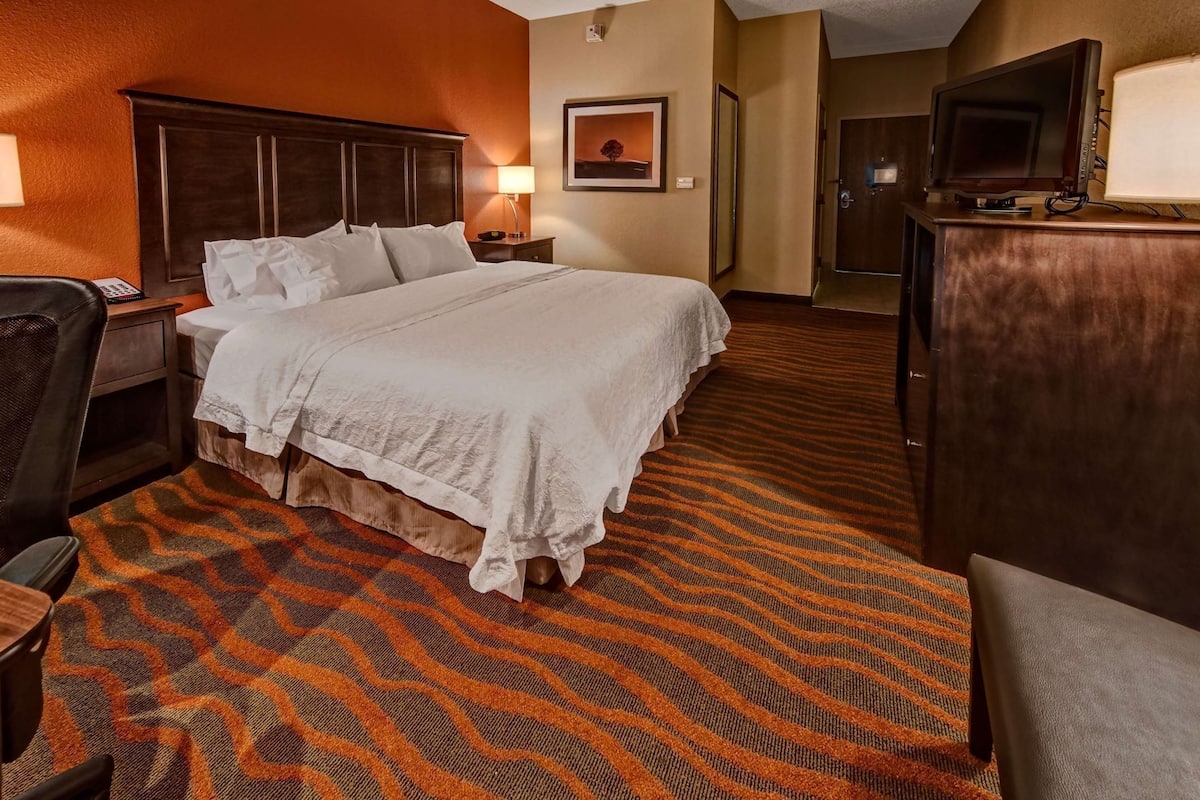 A hotel room with a large bed, a desk, a chair, a TV, and a door.