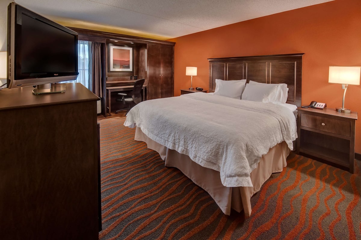A hotel room with a large bed, a desk with a chair, a television, two bedside lamps, and a telephone.