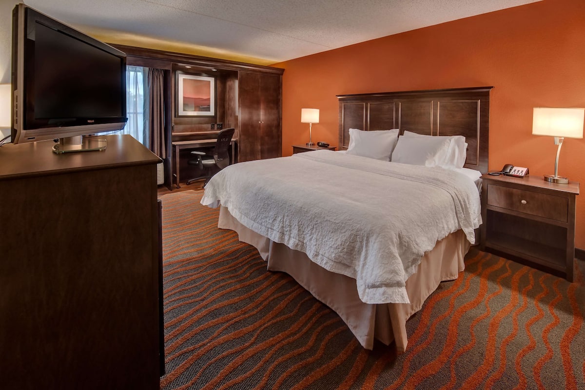 A hotel room with a large bed, a desk with a chair, a television, and two bedside lamps.