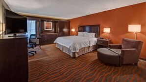 Una camera d'albergo con un letto grande, una scrivania con televisore, una sedia e pavimento rivestito di moquette.