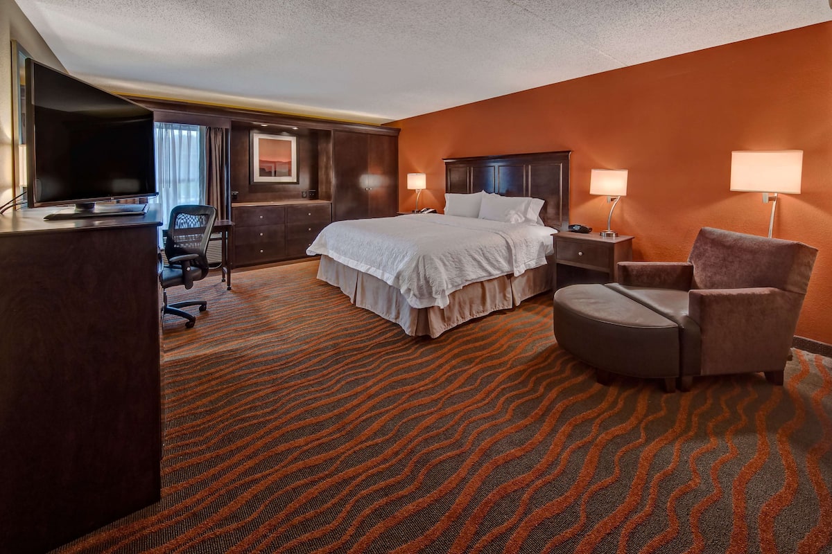 A hotel room with a large bed, a desk with a TV, a chair, and a carpeted floor.