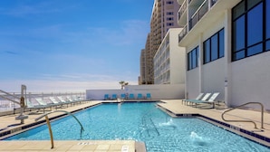 Una piscina al terrat amb aigua blava cristal·lina, gandules i un edifici alt al fons.