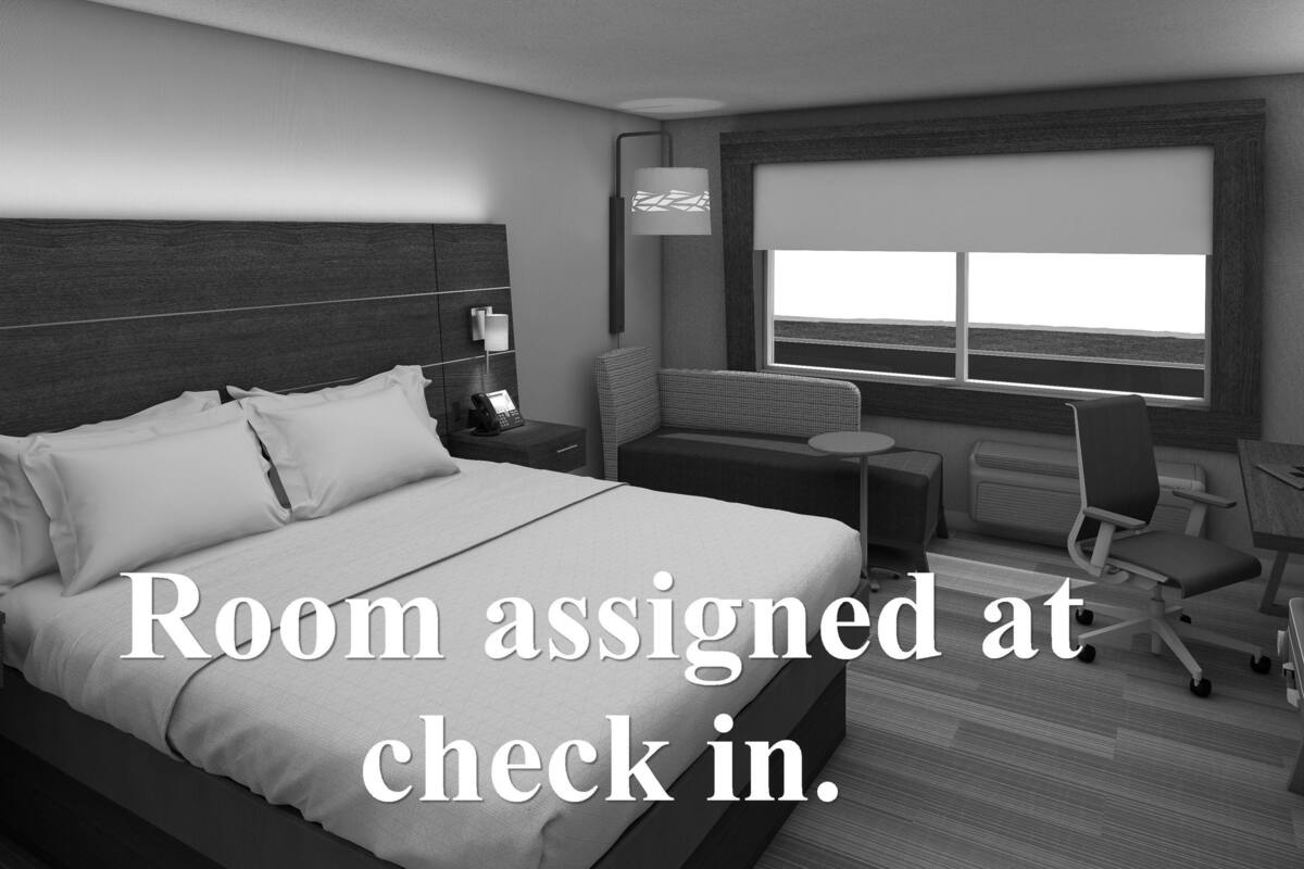 A hotel room with a bed, bedside table, lamp, chair, desk, and a window with a view.