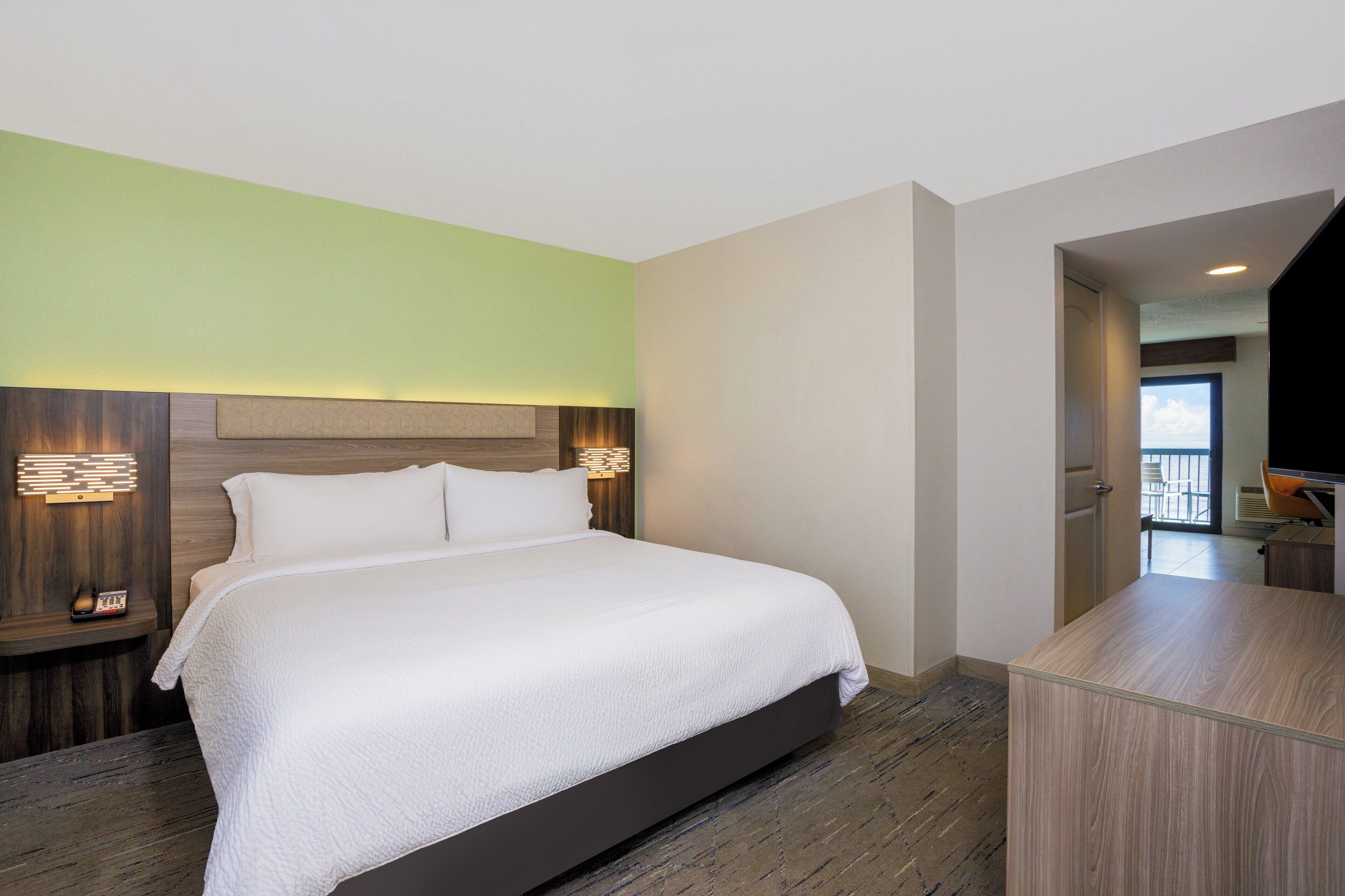Quarto de hotel com uma cama grande, mesa de cabeceira com abajur e vista para a varanda.