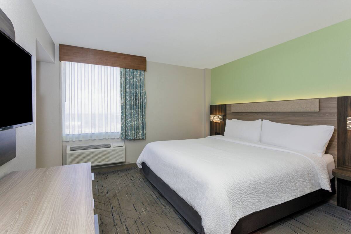 A hotel room with a large bed, a flat-screen TV, a desk, and a window with curtains.