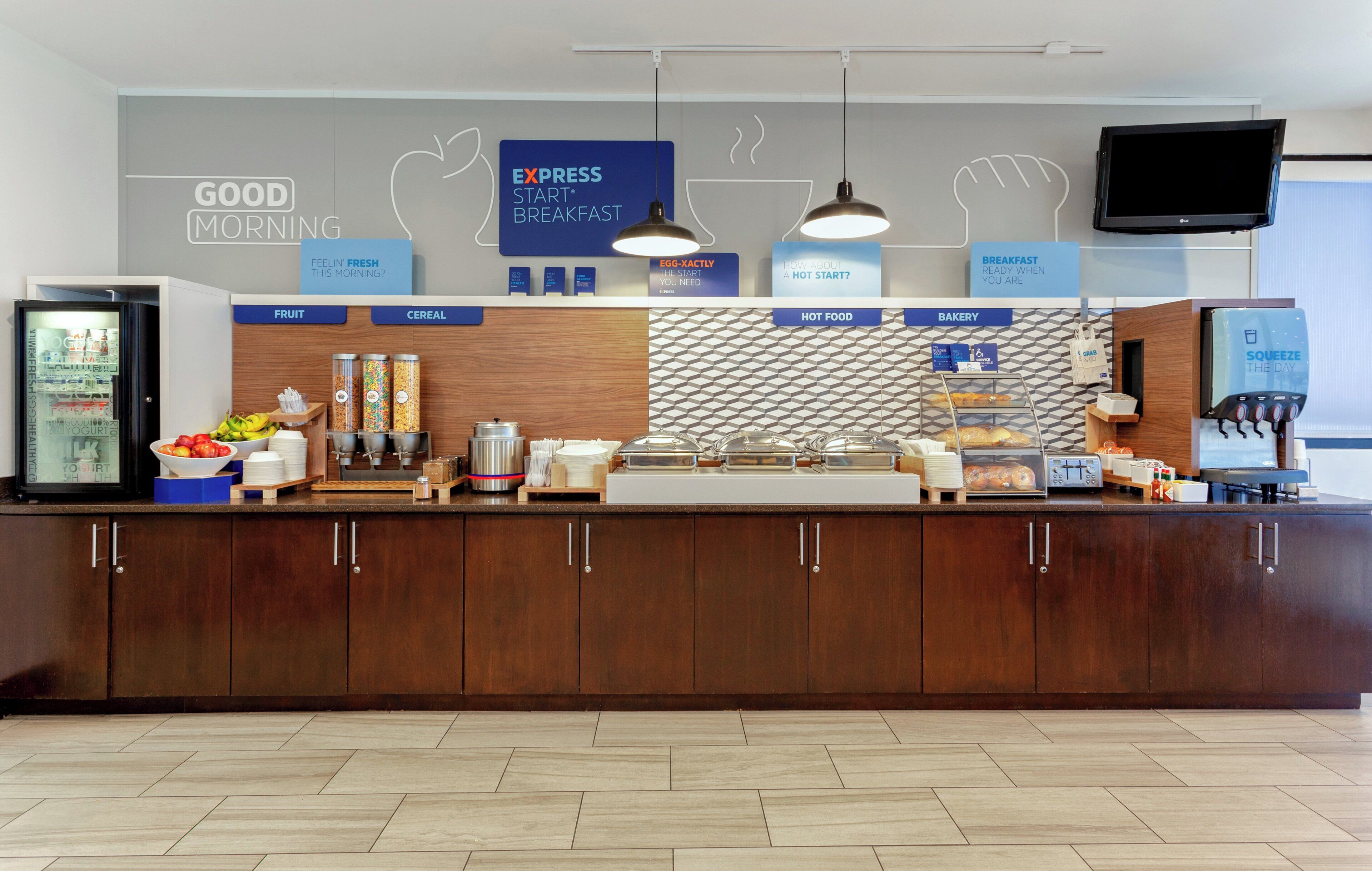 A breakfast area with a refrigerator, fruit and cereal dispensers, a hot food station, and a bakery section.