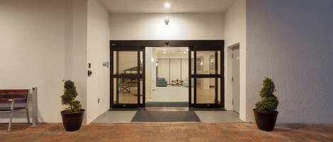 A hotel entrance with a brick floor, two potted plants, a bench, and a door leading inside.