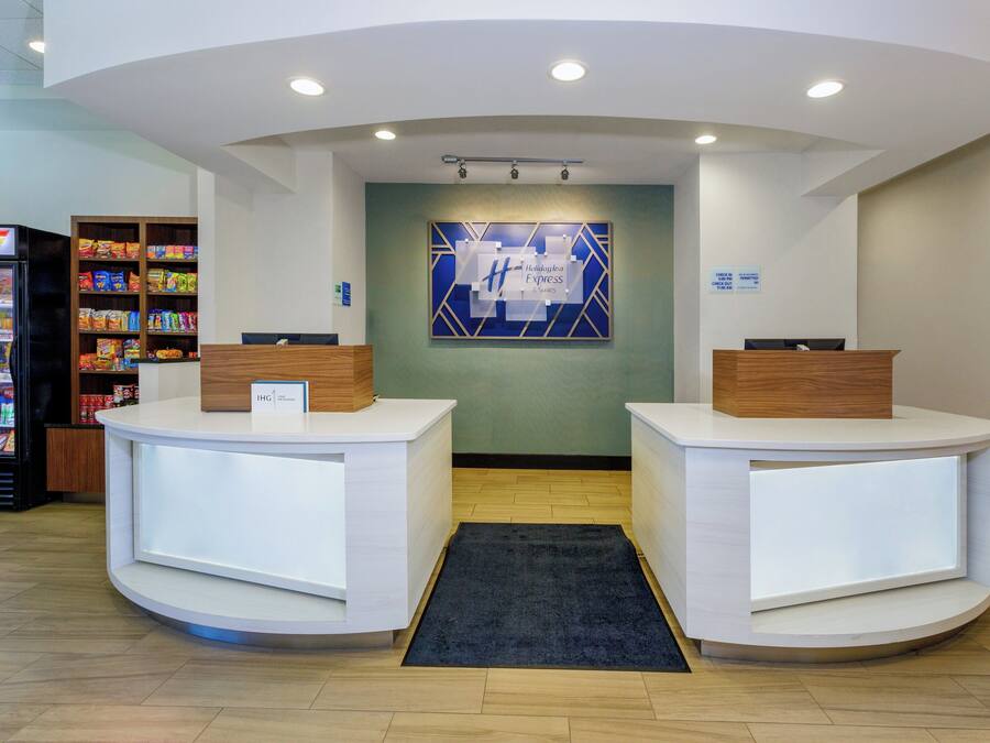 A reception area with two white reception desks, a blue and white wall art piece, a refrigerator stocked with snacks, and a wooden shelf with various items.