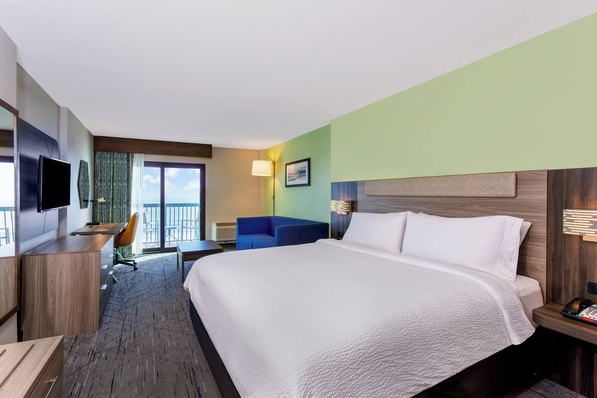 A hotel room with a large bed, a desk with a chair, a TV, and a balcony with a view.