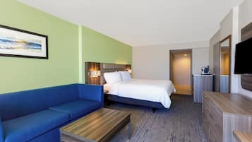 Une chambre d’hôtel avec un canapé bleu, un lit avec une literie blanche, une table basse en bois, une commode et un téléviseur à écran plat.