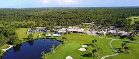 Vista aérea de un campo de golf con un club de campo, piscina y un extenso cuerpo de agua.