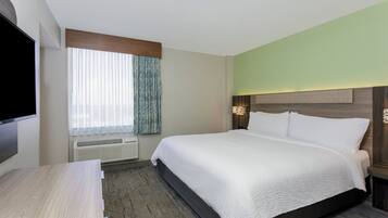 A hotel room with a large bed, a flat-screen TV, a desk, and a window with curtains.