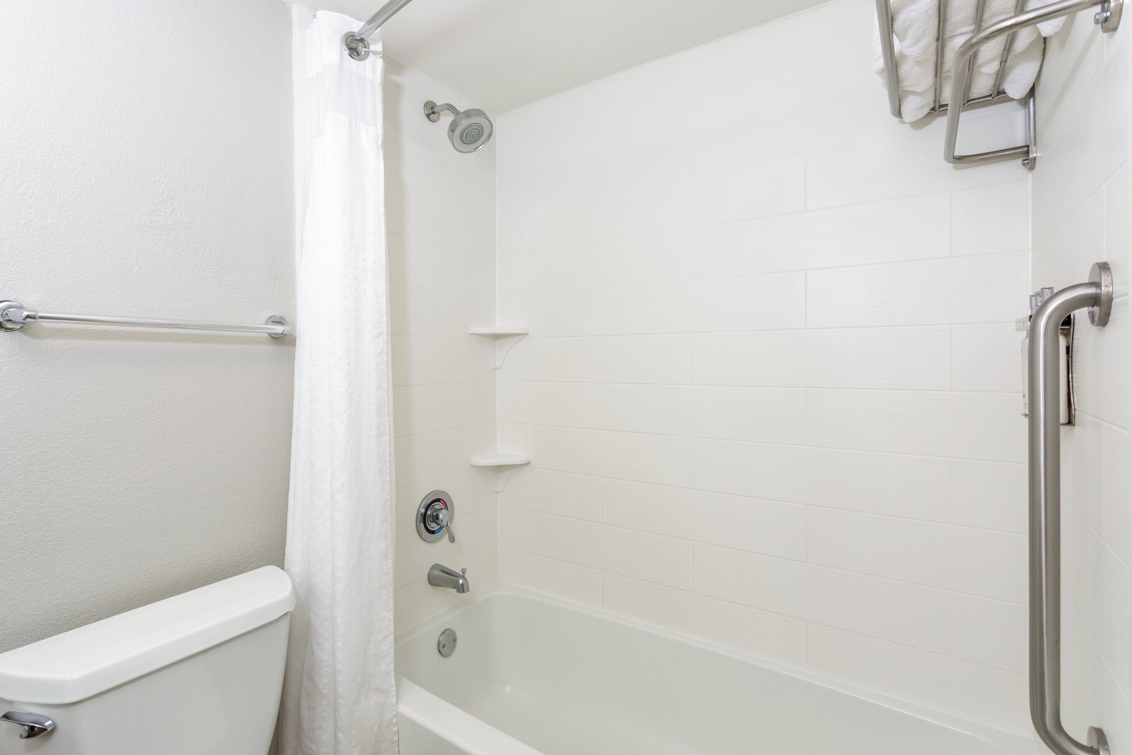 A white bathroom with a bathtub, a showerhead, and a toilet.