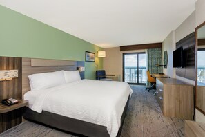 A hotel room with a large bed, a desk, a chair, a TV, and a balcony with a view of the ocean. - Holiday Inn Express & Suites Oceanfront by IHG (Daytona Beach Shores)