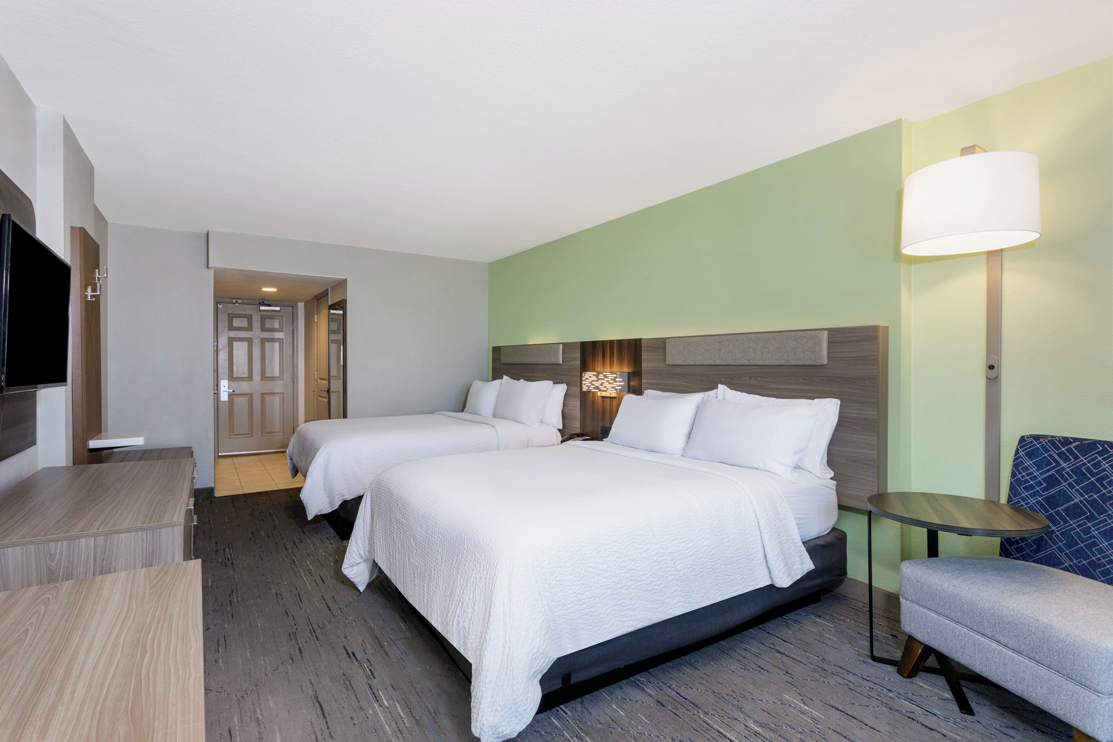 Quarto de hotel com duas camas, televisão, escrivaninha, cadeira e abajur.