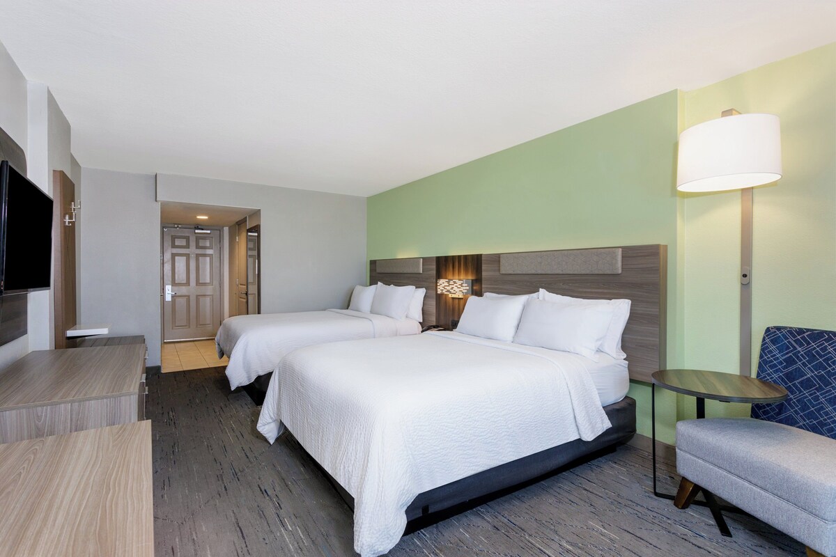A hotel room with two beds, a TV, a desk, a chair, and a lamp.