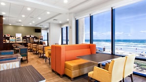 Un restaurant modern amb vista a la platja, amb seients taronja, taules de fusta i diversos seients.