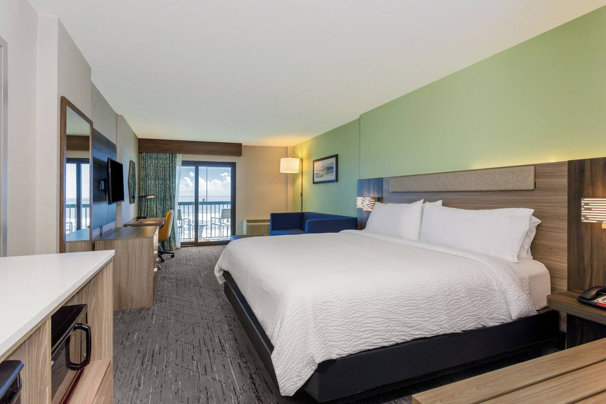 A hotel room with a bed, desk, chair, and a view of the outdoors.