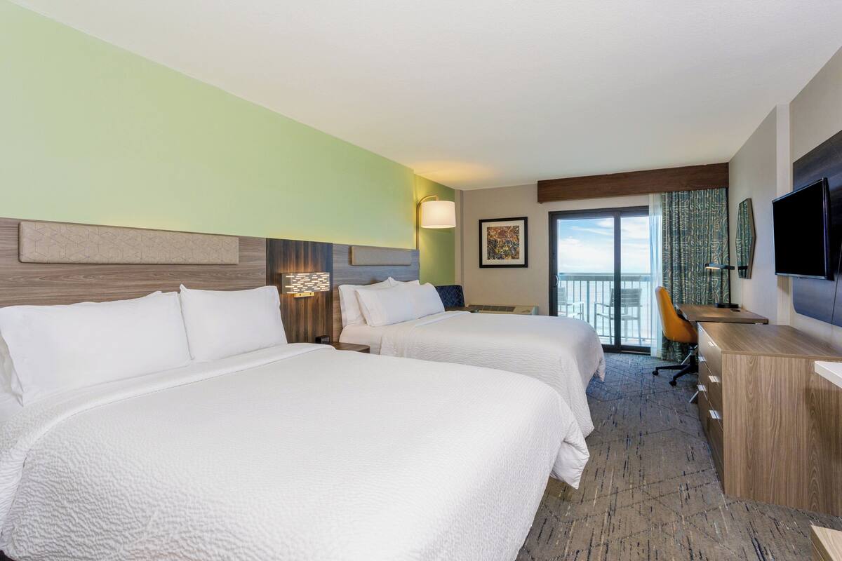 A hotel room with two beds, a desk, a chair, and a TV.