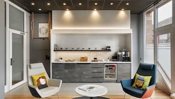 A modern living room with two chairs, a coffee table, and a kitchen area with a refrigerator and coffee machine.