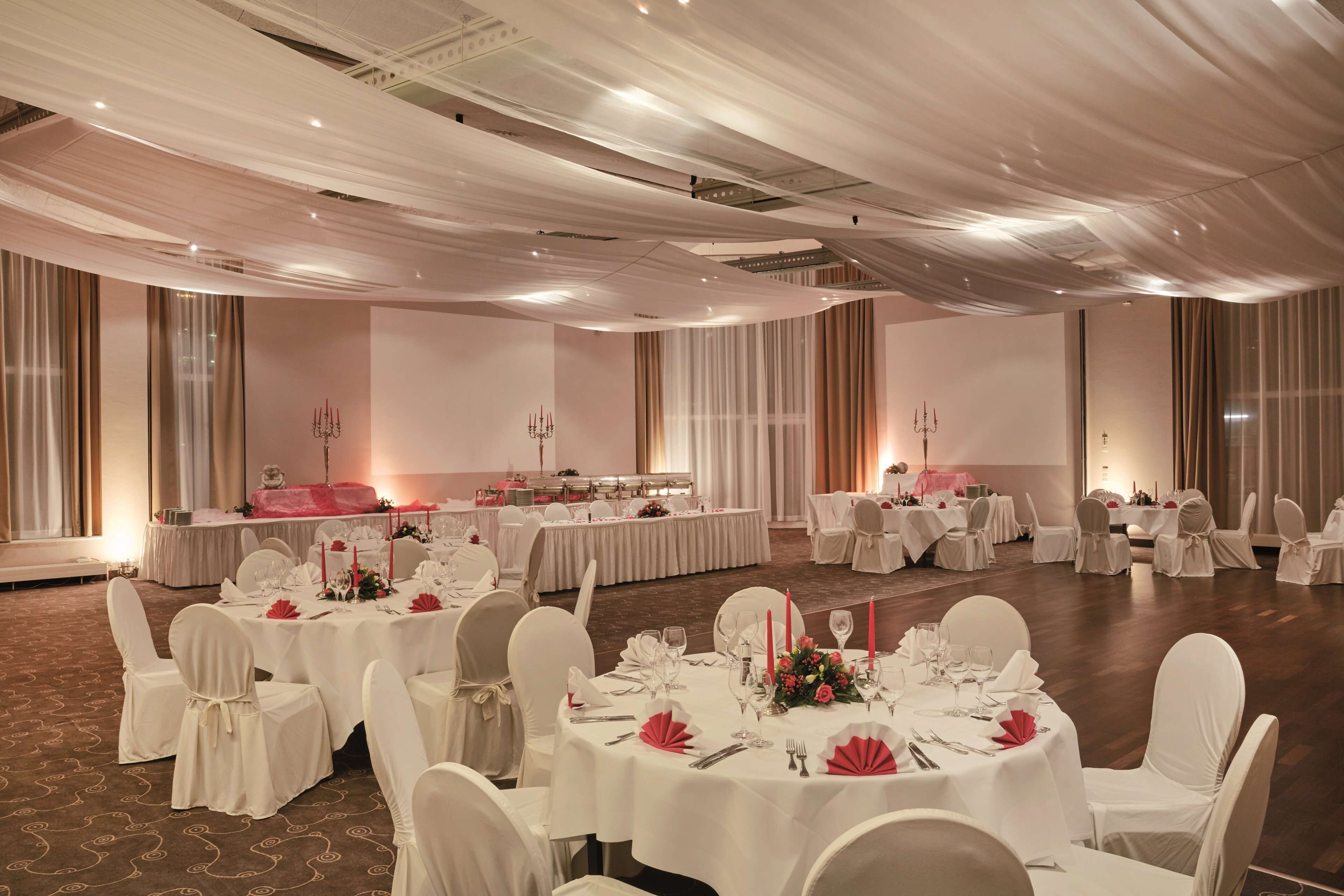 A banquet hall with round tables set for dining, white chairs, and a buffet area.