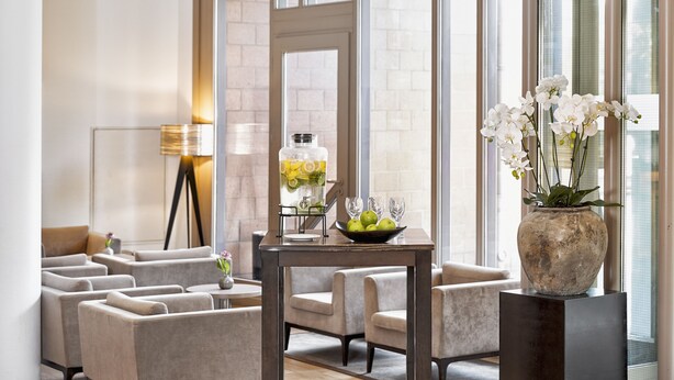 Un moderno vestíbulo de hotel con zona de estar, un jarrón grande con flores blancas y una mesa con frutero y vasos.