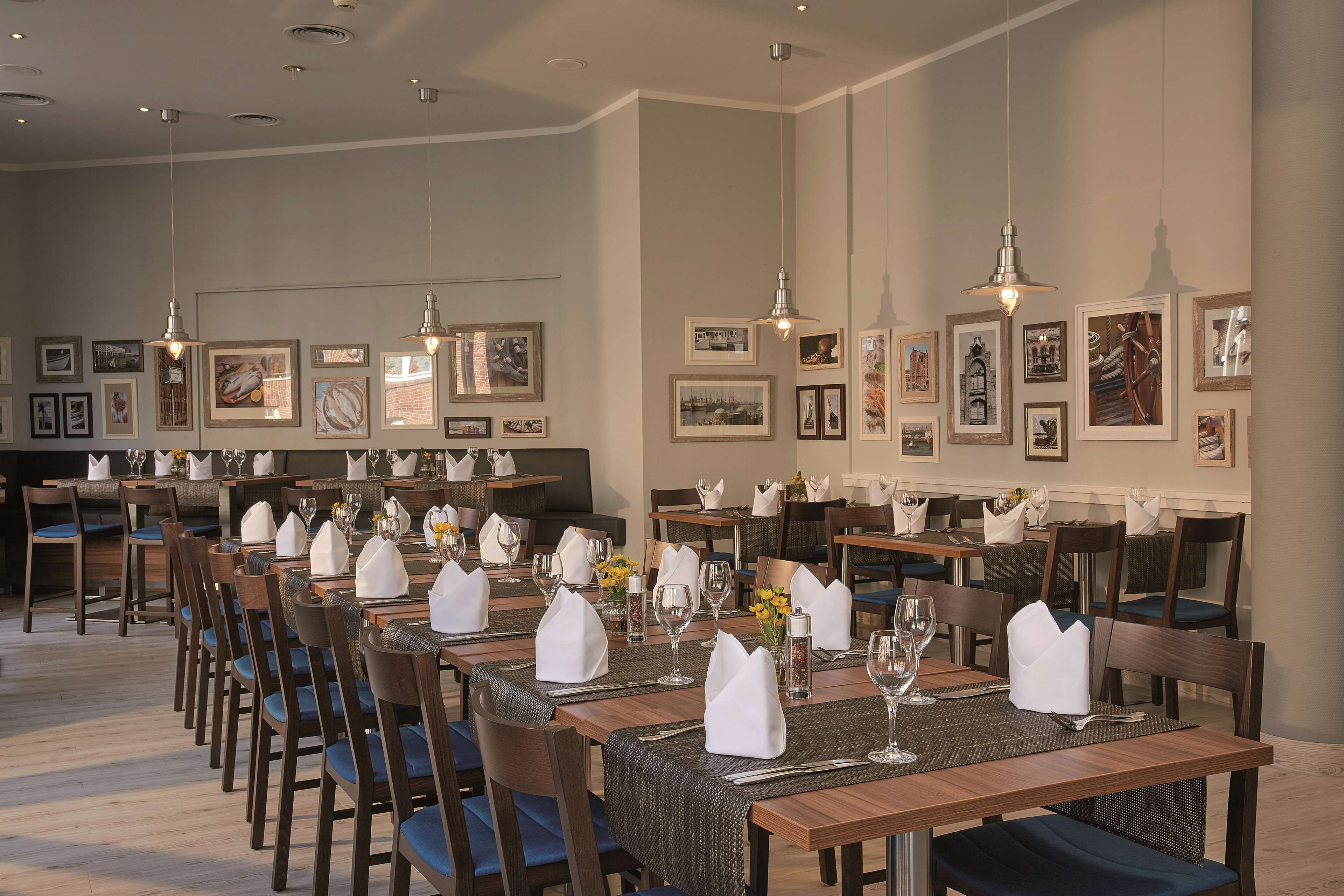 A dining area with multiple tables set for service, wooden chairs, and framed artwork on the walls.