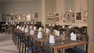 A dining area with multiple tables set for service, wooden chairs, and framed artwork on the walls.