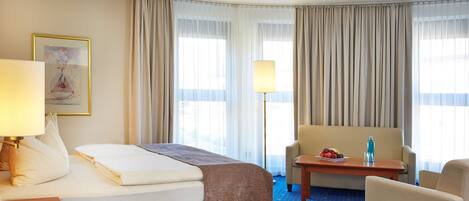 Ein Hotelzimmer mit Bett, Schreibtisch, Stuhl, Lampe und einem Gemälde an der Wand.