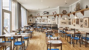 Un restaurante espacioso con mesas de madera y sillas con cojines azules, ventanas amplias y decoración temática náutica.