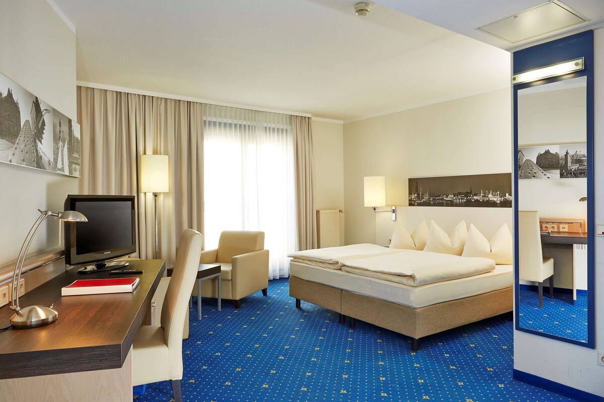 A hotel room with a bed, desk, chair, television, and a large mirror.