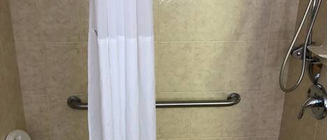 A shower area with a grab bar, a white chair, and a white shower curtain.