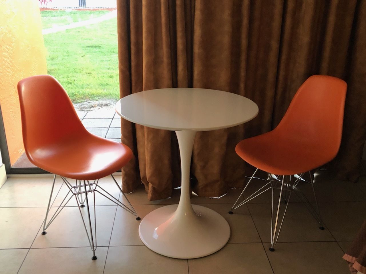 A dining area with a round table and two orange chairs with metal legs.