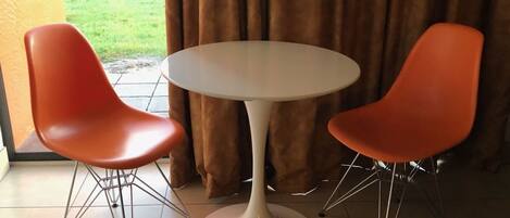 A dining area with a round table and two orange chairs with metal legs.