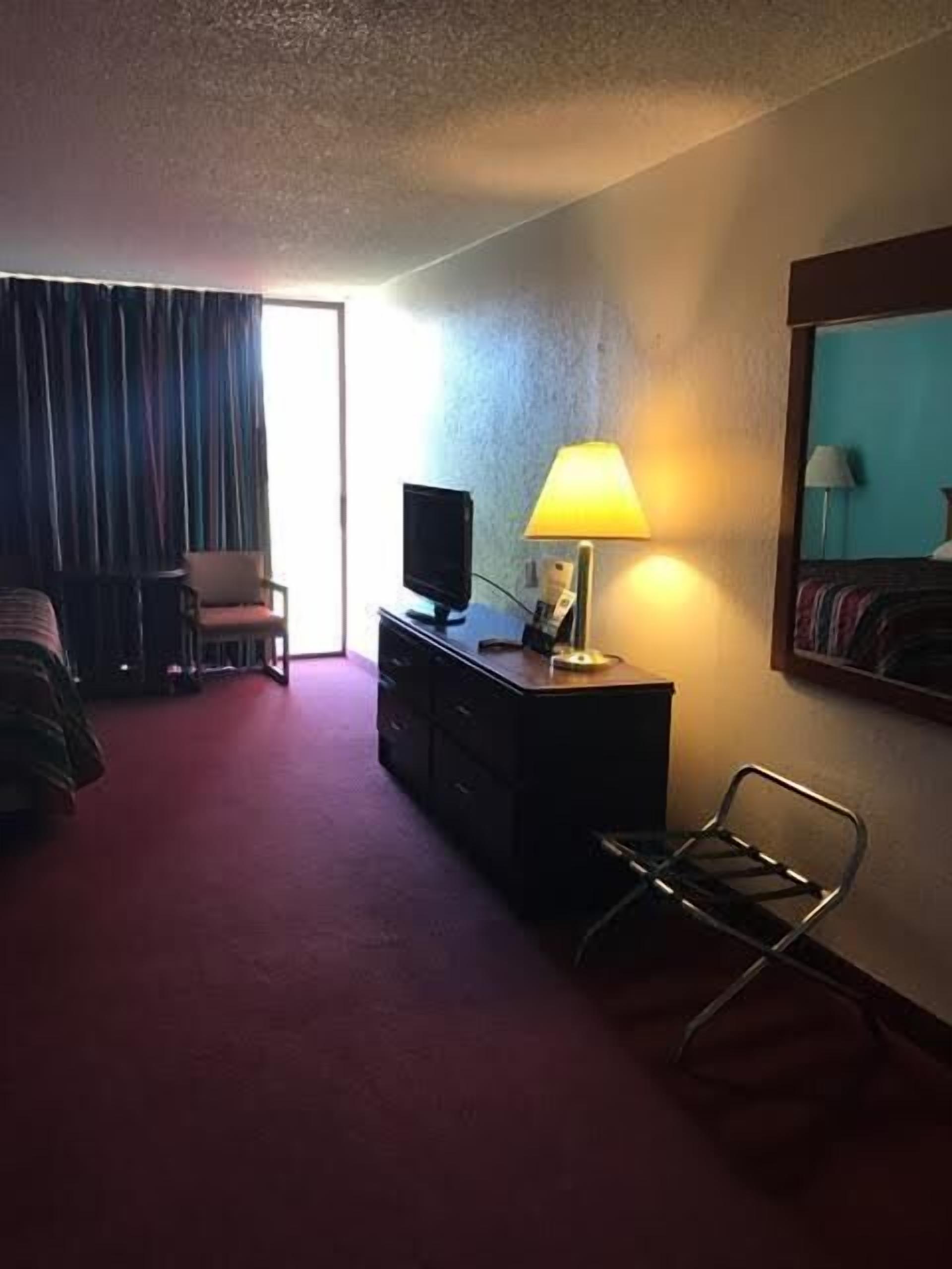 A hotel room with a bed, a desk with a lamp, a chair, and a television.