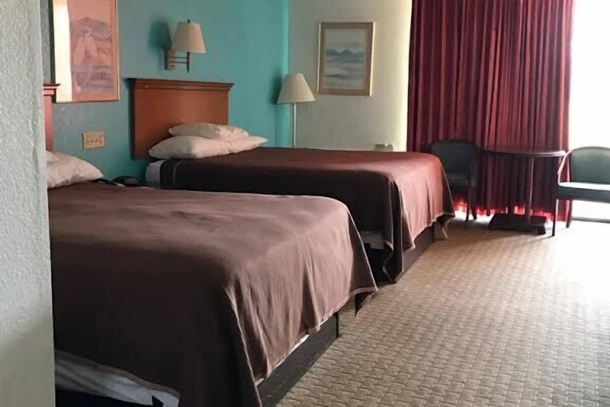Une chambre d’hôtel avec deux lits, une tête de lit en bois, un rideau rouge et un sol carrelé.