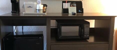 A hotel room desk with a flat-screen TV, a coffee maker, a microwave, and a mini fridge.