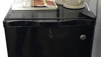 A compact black refrigerator with a coffee maker on top, a glass container, and a white cup.