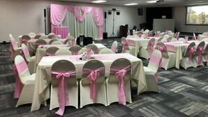 A conference room with tables and chairs, pink sashes, and a stage with drapes. - Howard Johnson by Wyndham Winter Haven FL (Winter Haven)